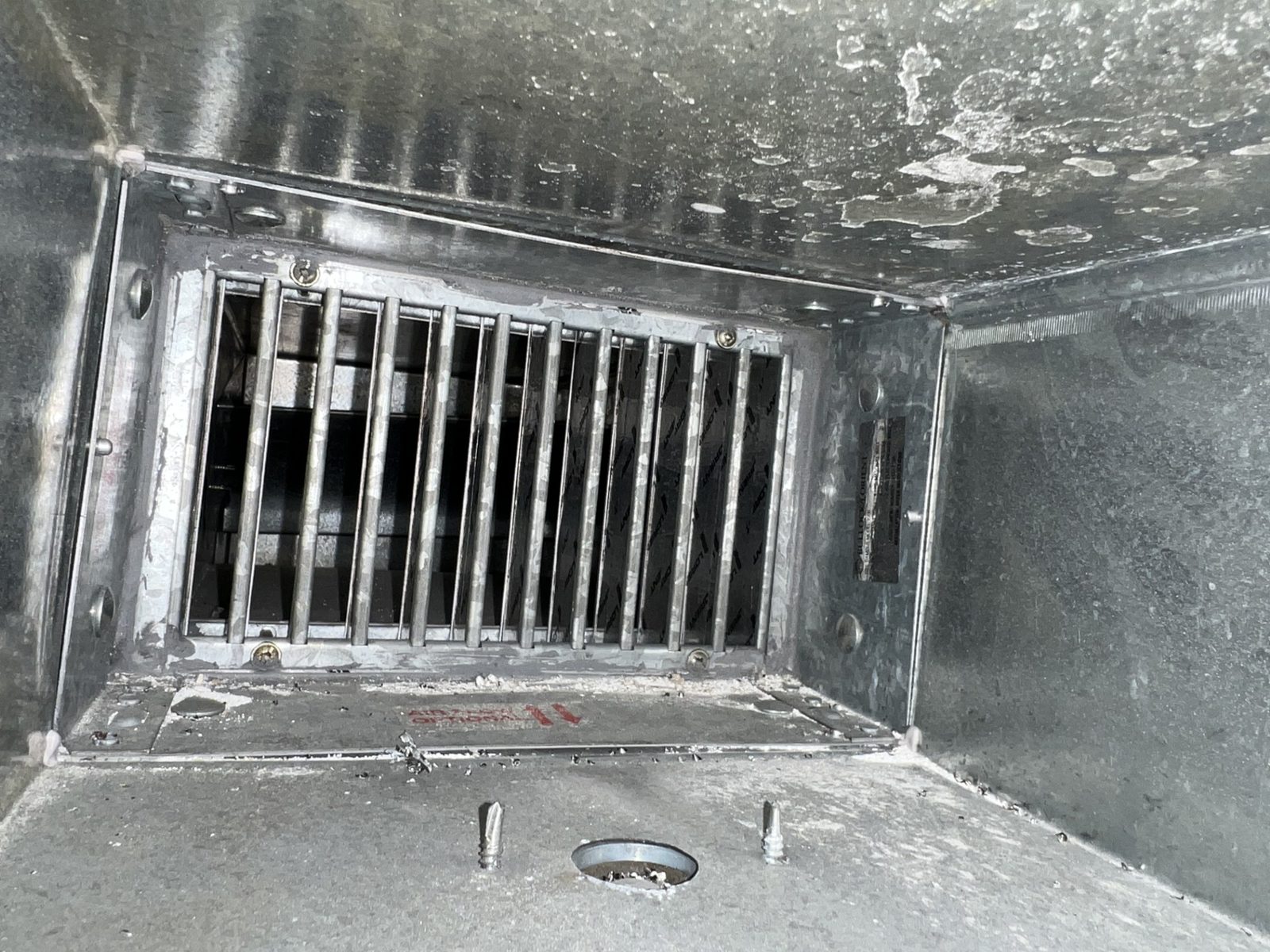 Internal view of an installed curtain fire damper showing folding blade assembly and fusible link in HVAC ductwork